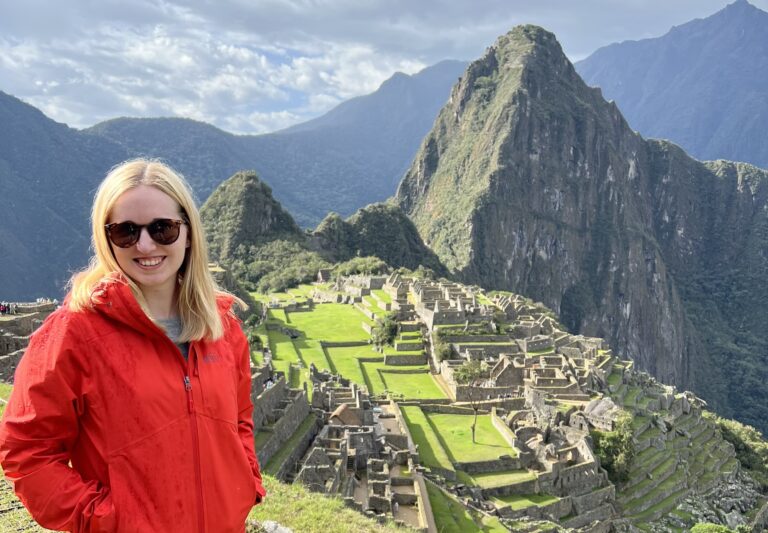 Jackie Swayze smiling in front of Machu Picchu wearing a red rain coat